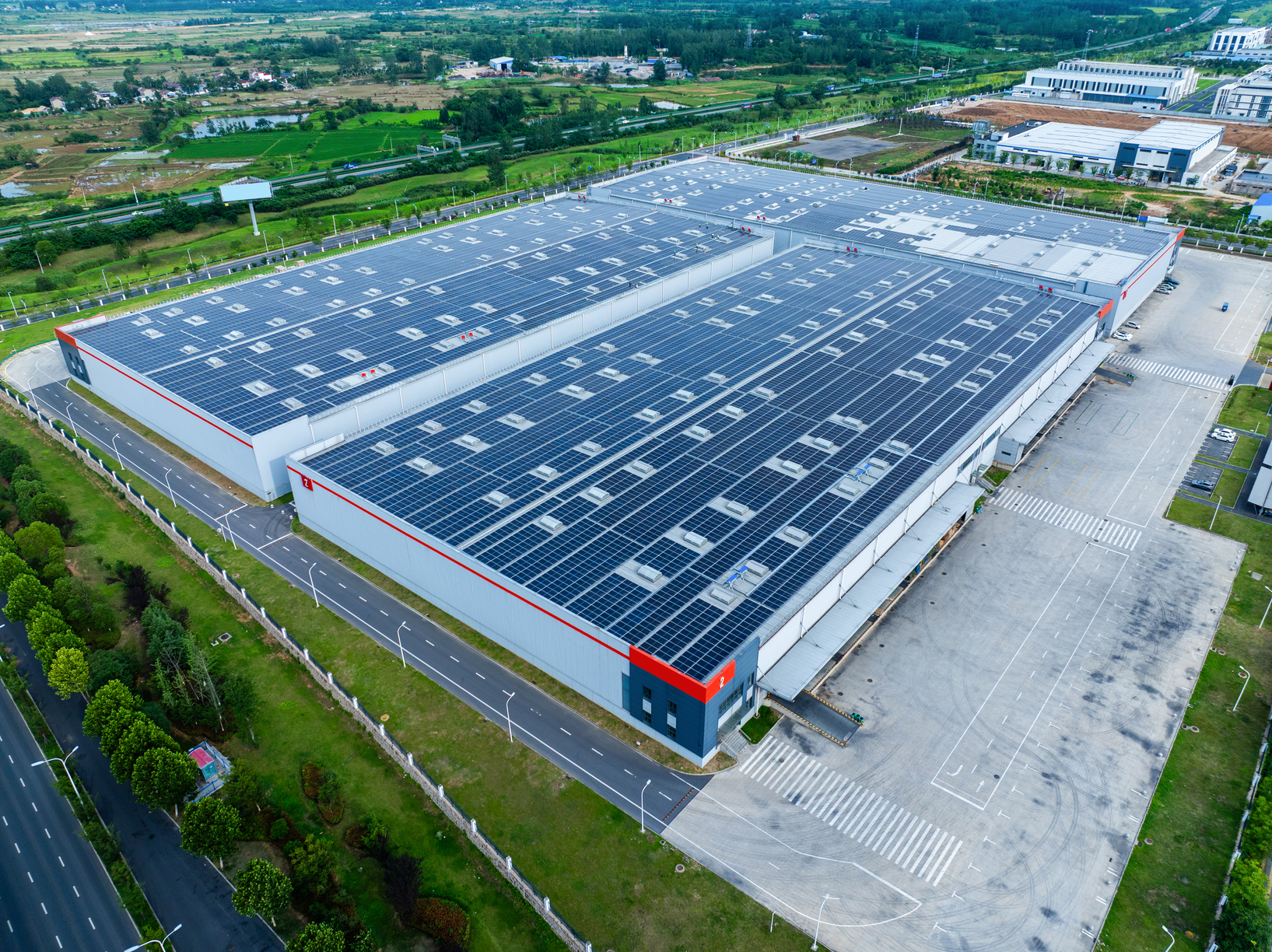 A vertical aerial shot of a factory with solar panels on the roof, showcasing transport trucks and industrial infrastructure.